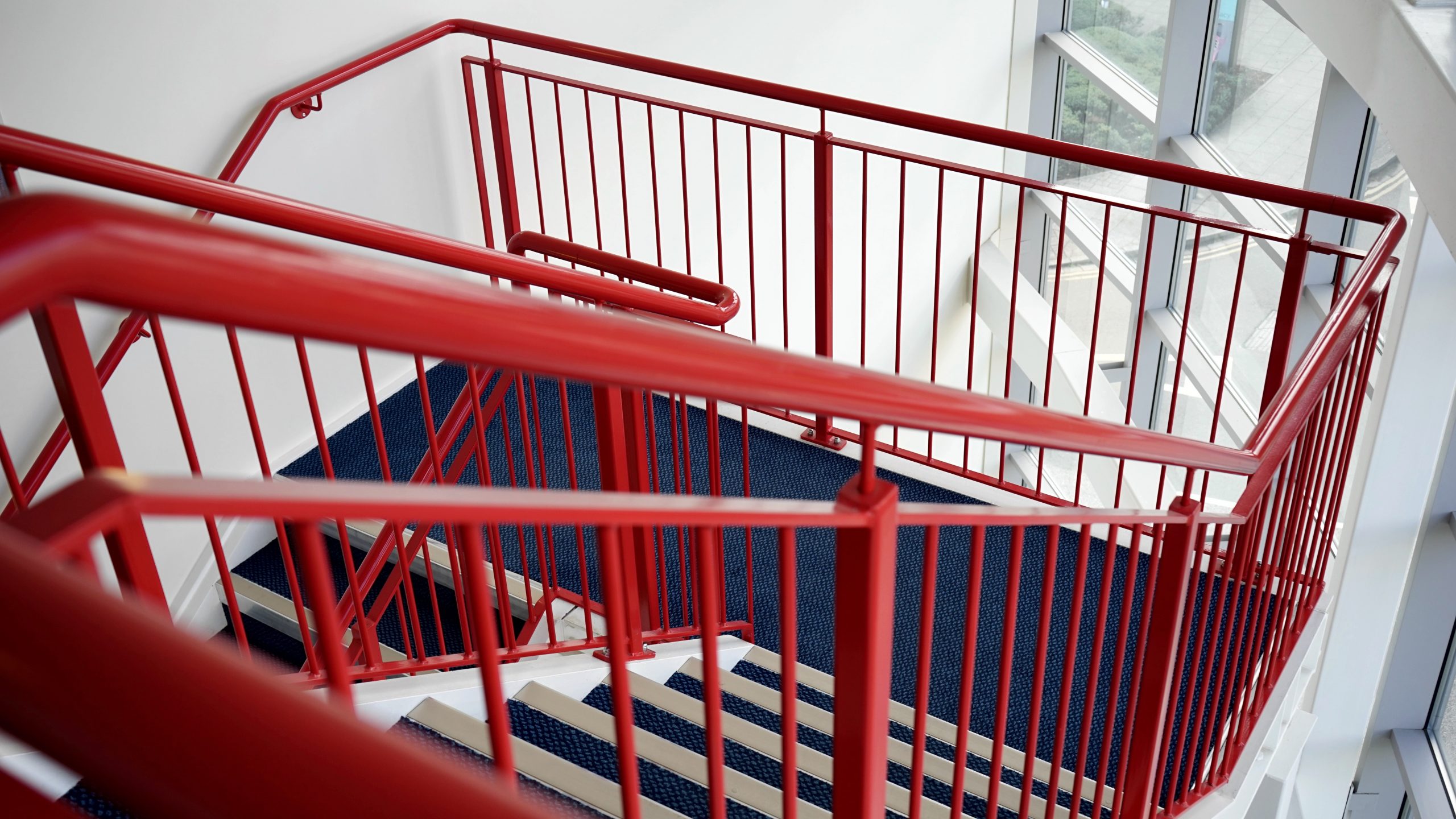 Das Bild zeigt eine Treppe mit rotem Teppich und rotem Geländer