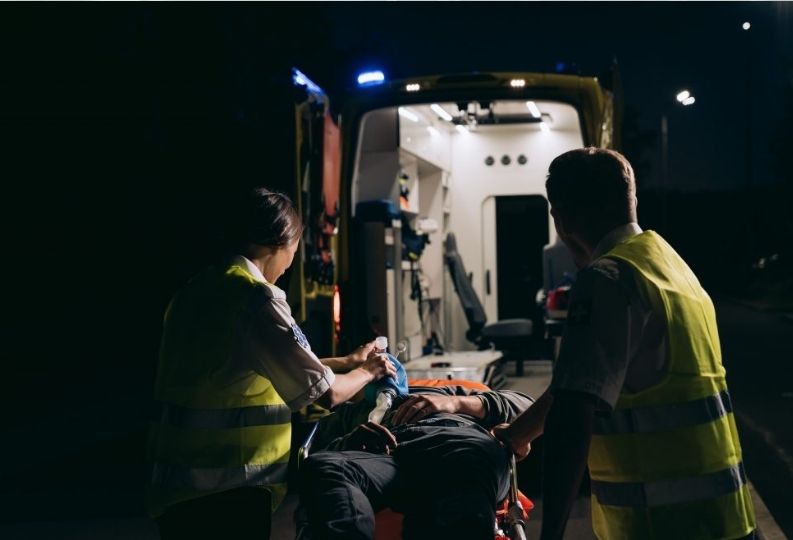 Sanitäter schieben einen Mann nach einem Unfall in den Krankenwagen. Es ist nachts. 